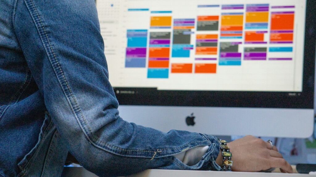 A person is sitting behind an Apple computer with a calendar app open - DevTeam.Space