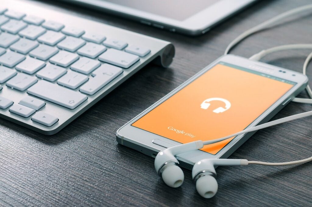 a cell phone lies next to a computer keyboard with ear buds connected - DevTeam.Space